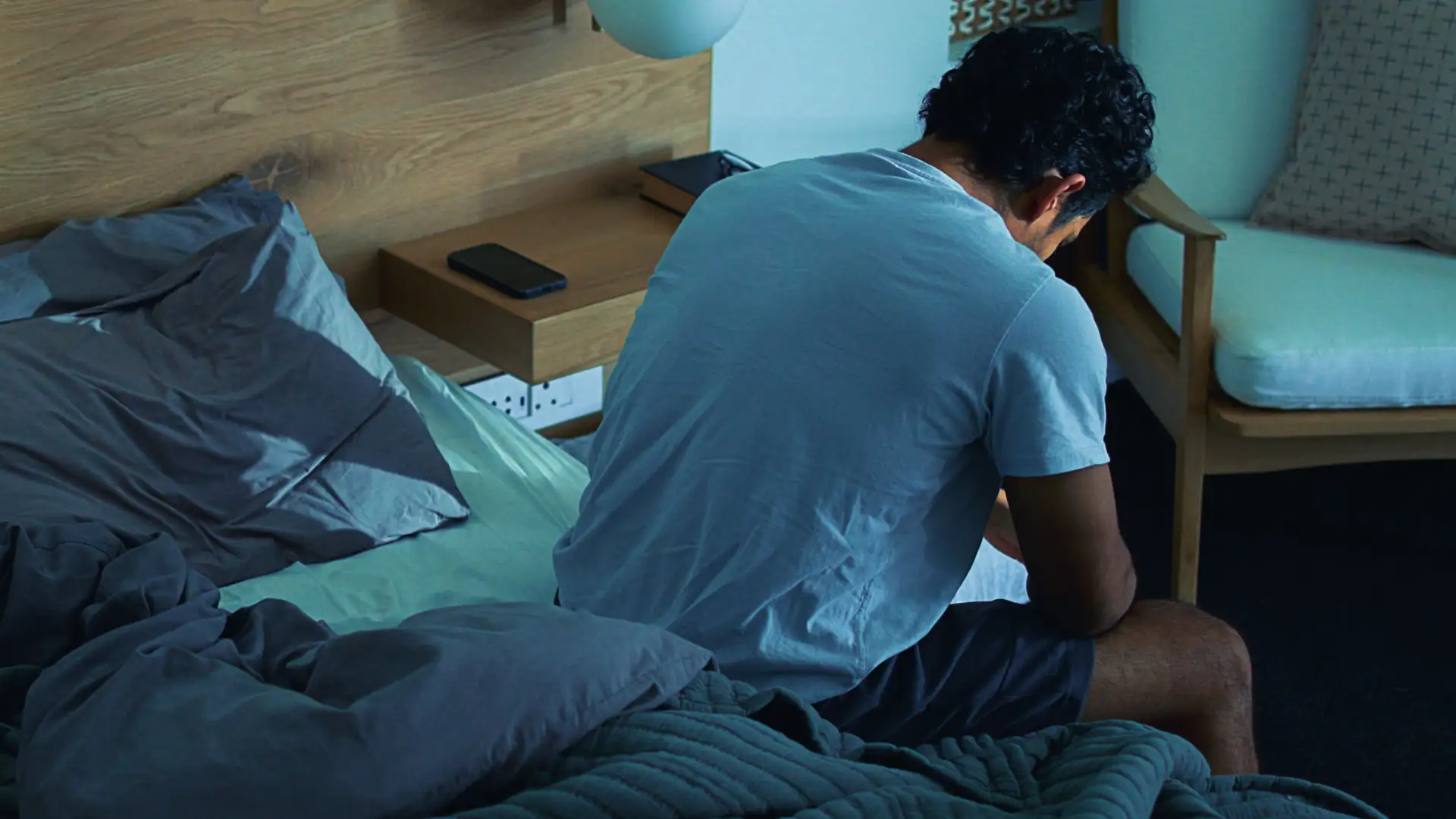 Erschöpfter Mann sitzt zusammengesunken auf einem Bett als Symbolbild für Chronisches Fatigue-Syndrom, Long Covid und schwere Erschöpfung.