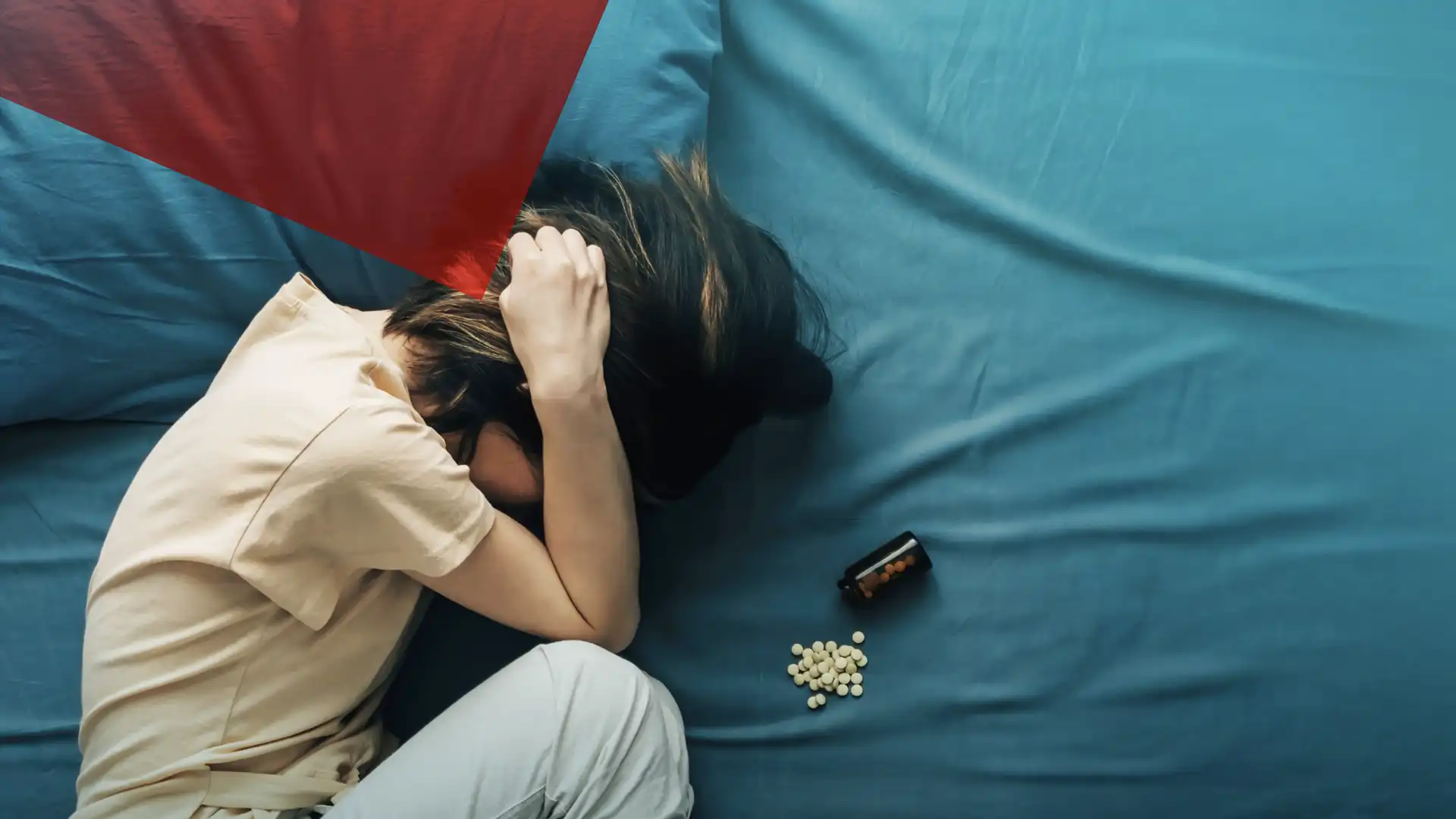 Frau liegt mit starken Kopfschmerzen im Bett, hält den Kopf, neben ihr liegen Tabletten – Symbolbild für Migräne und Schmerzbelastung.